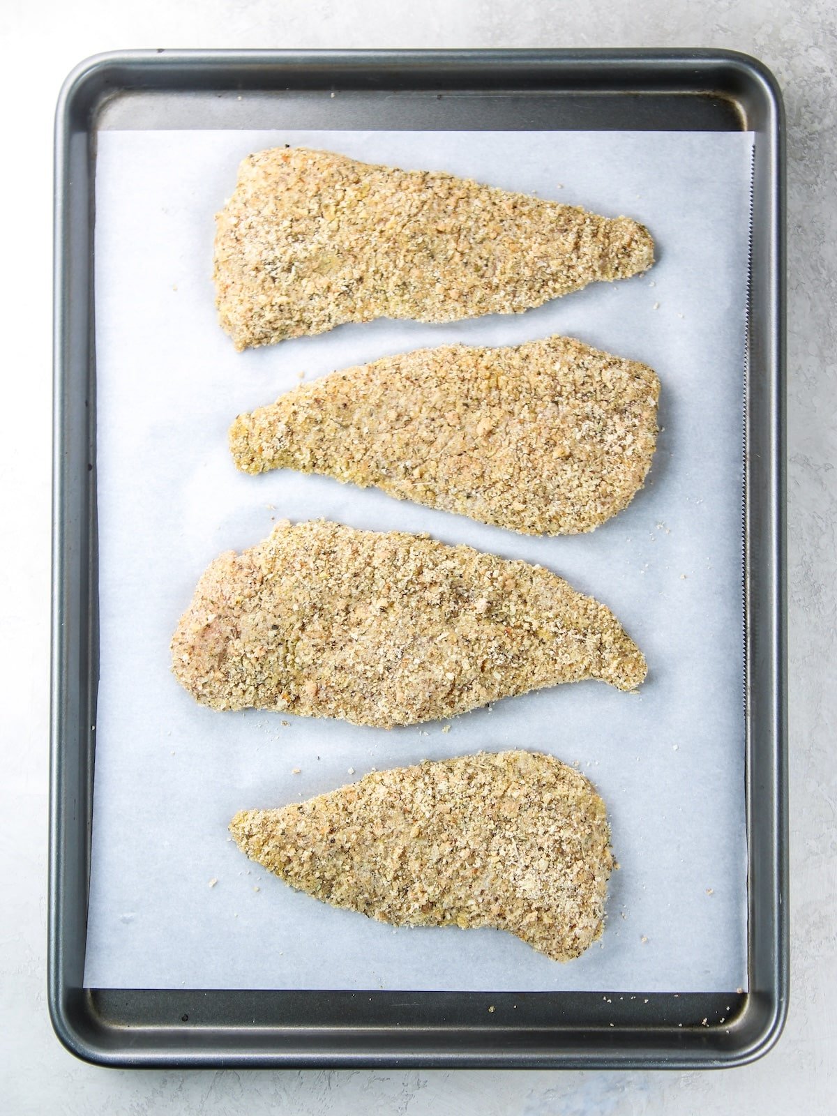 Low Carb Chicken Parmesan on a baking sheet before cooking Chicken cutlets with breadcrumbs on a baking sheet ready to cook for Gluten-free Chicken Parmesan.