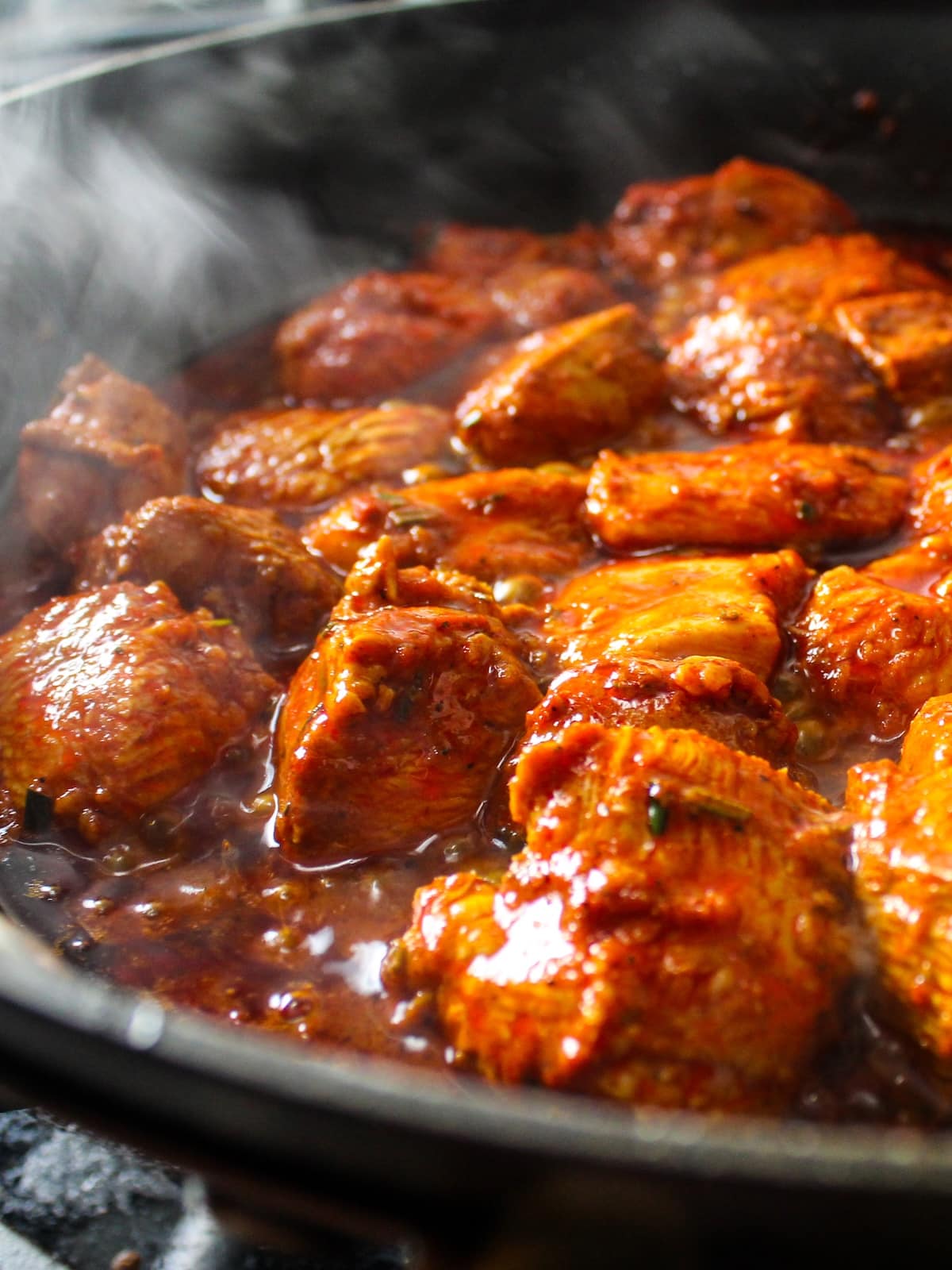 A eye-level photo of the cut up chicken and harissa paste marinade sauteing in a pan.