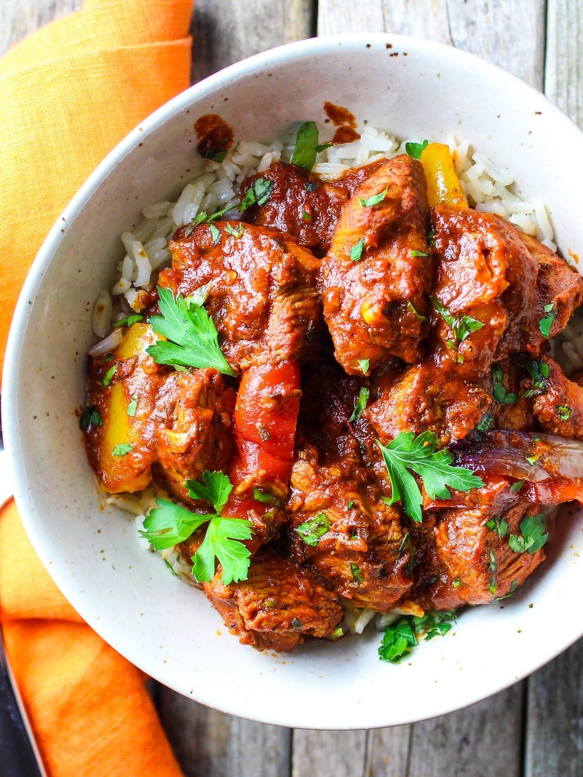 Lemon Harissa Chicken A bowl with the cooked harissa chicken recipe, peppers and onions, and garnished with fresh parsley.