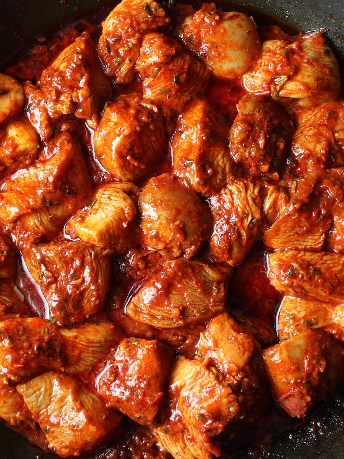 Harissa chicken sauteing in a pan on the stove top.