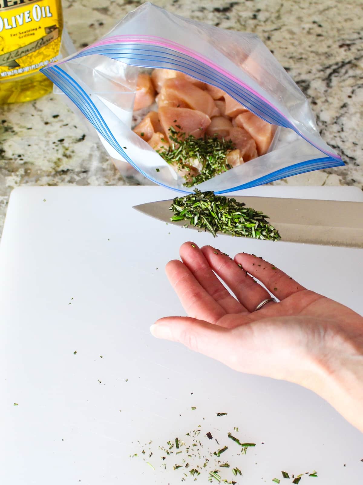 Adding fresh chopped Rosemary to a storage bag with the cut up chicken breasts.