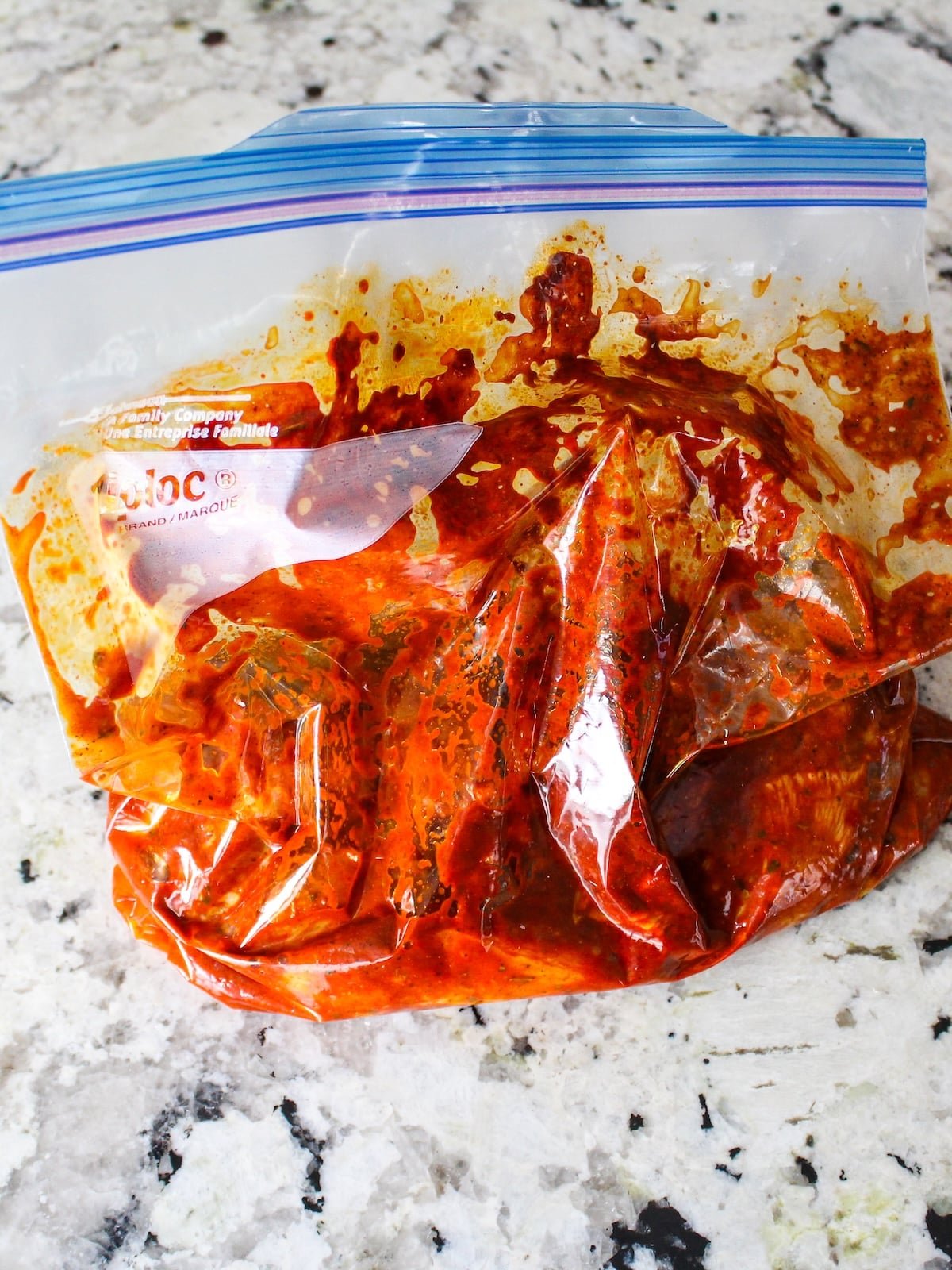 A storage bag with cut up boneless skinless chicken breasts covered in the lemon harissa marinade.