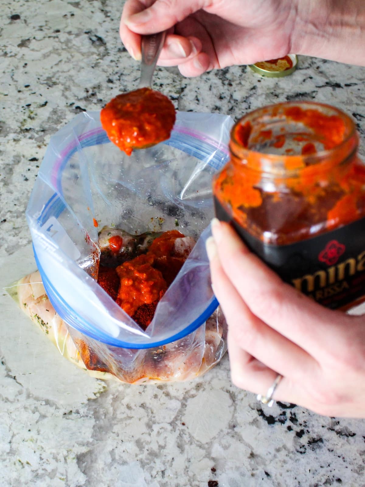 Spooning the harissa sauce to the marinade for the chicken.