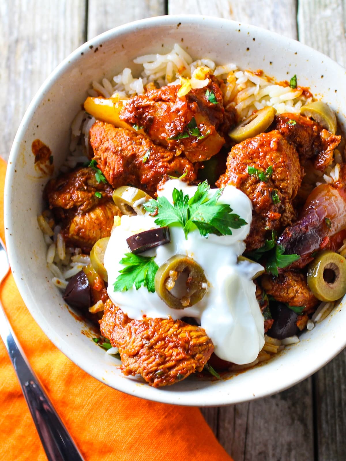 Lemon Harissa Chicken A bowl with jasmine rice topped with lemon harissa chicken, garnished with Greek yogurt, sliced olives, fresh parsley and capers.
