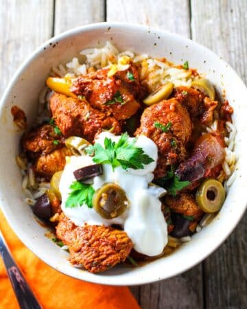 A 1200x1200 photo of a bowl with jasmine rice topped with delicious harissa chicken, garnished with Greek yogurt, sliced olives, and fresh parsley.
