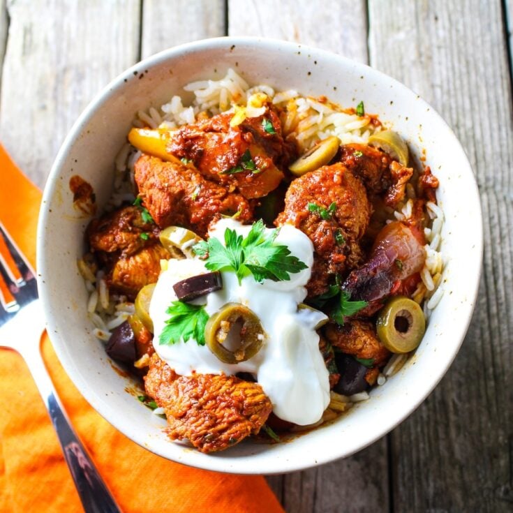 A 1200x1200 photo of a bowl with jasmine rice topped with delicious harissa chicken, garnished with Greek yogurt, sliced olives, and fresh parsley.