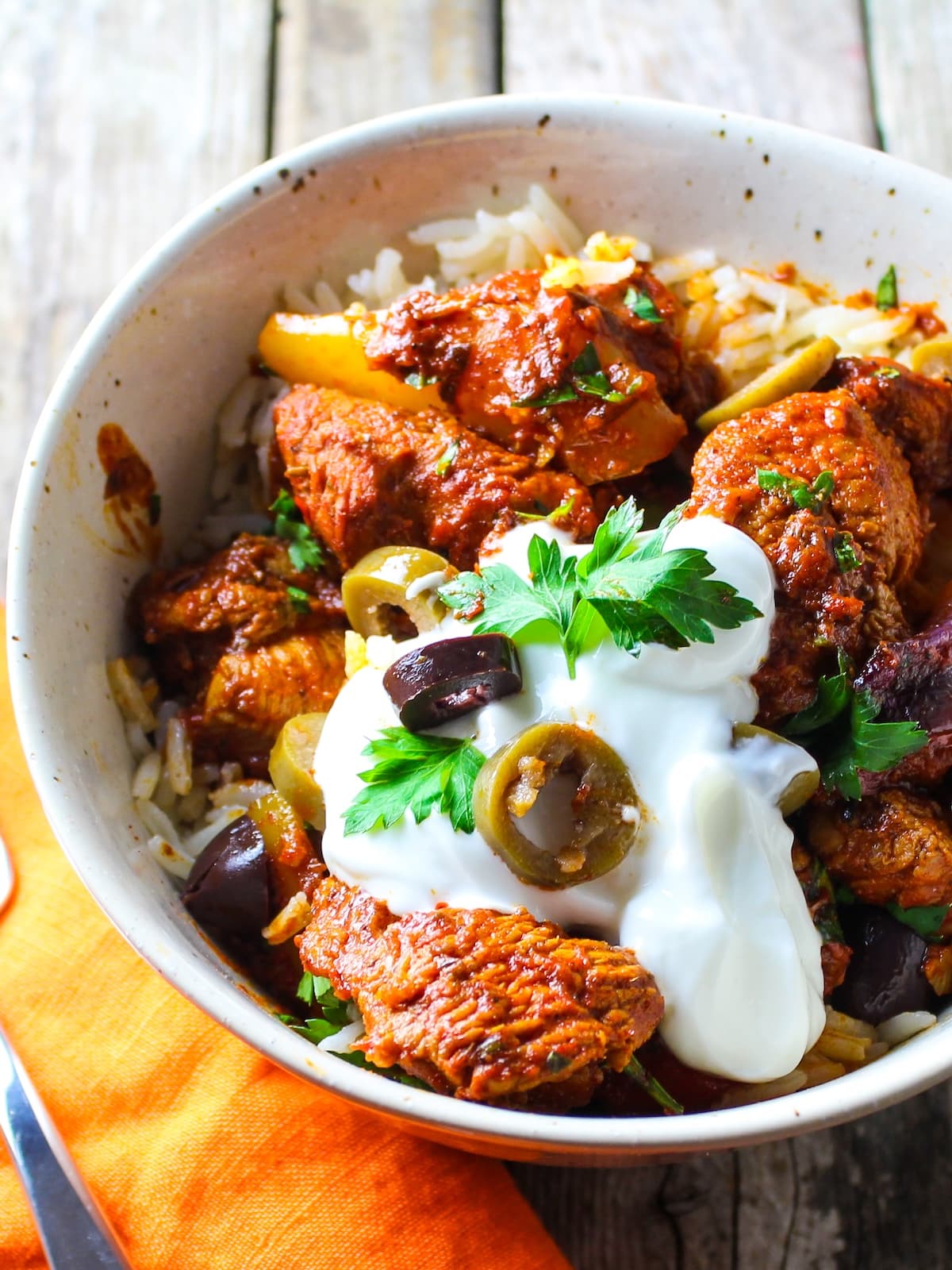 A bowl with jasmine rice topped with delicious harissa chicken, garnished with Greek yogurt, sliced olives, and fresh parsley.