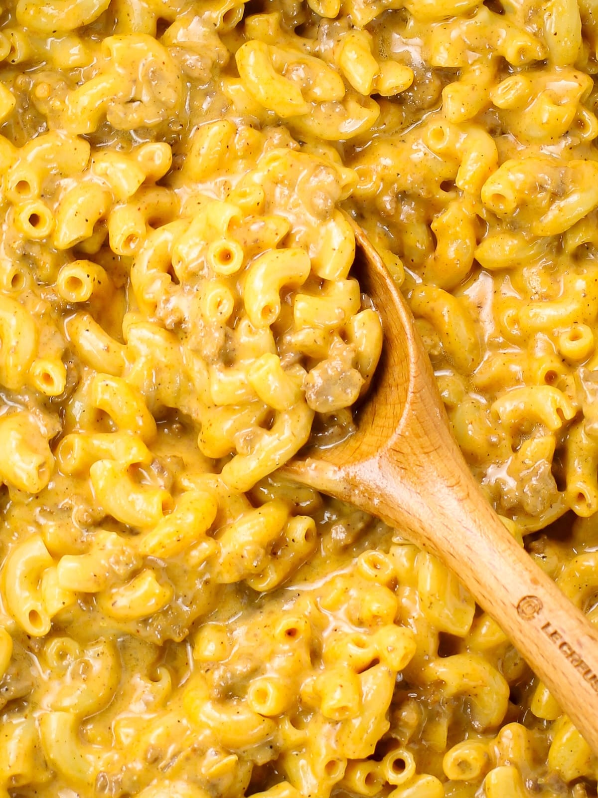 A large pot with a wooden spoon with homemade cheeseburger macaroni.