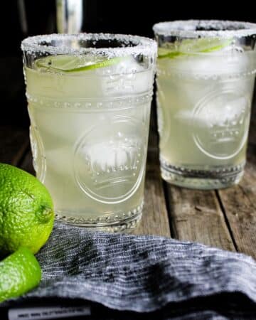 Two Elderflower Margaritas with lime wedges and St. Germain Liqueur in the background