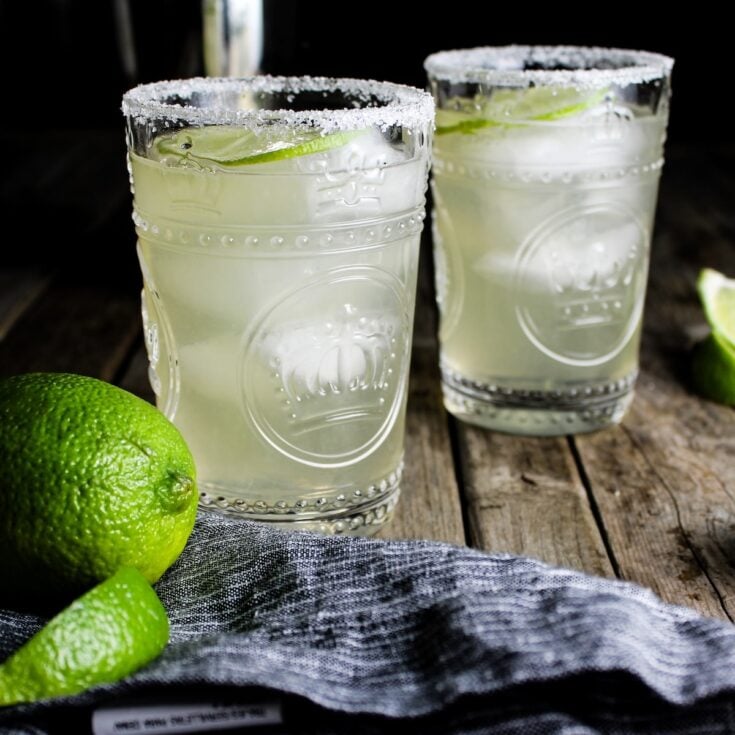 Two Elderflower Margaritas with lime wedges and St. Germain Liqueur in the background