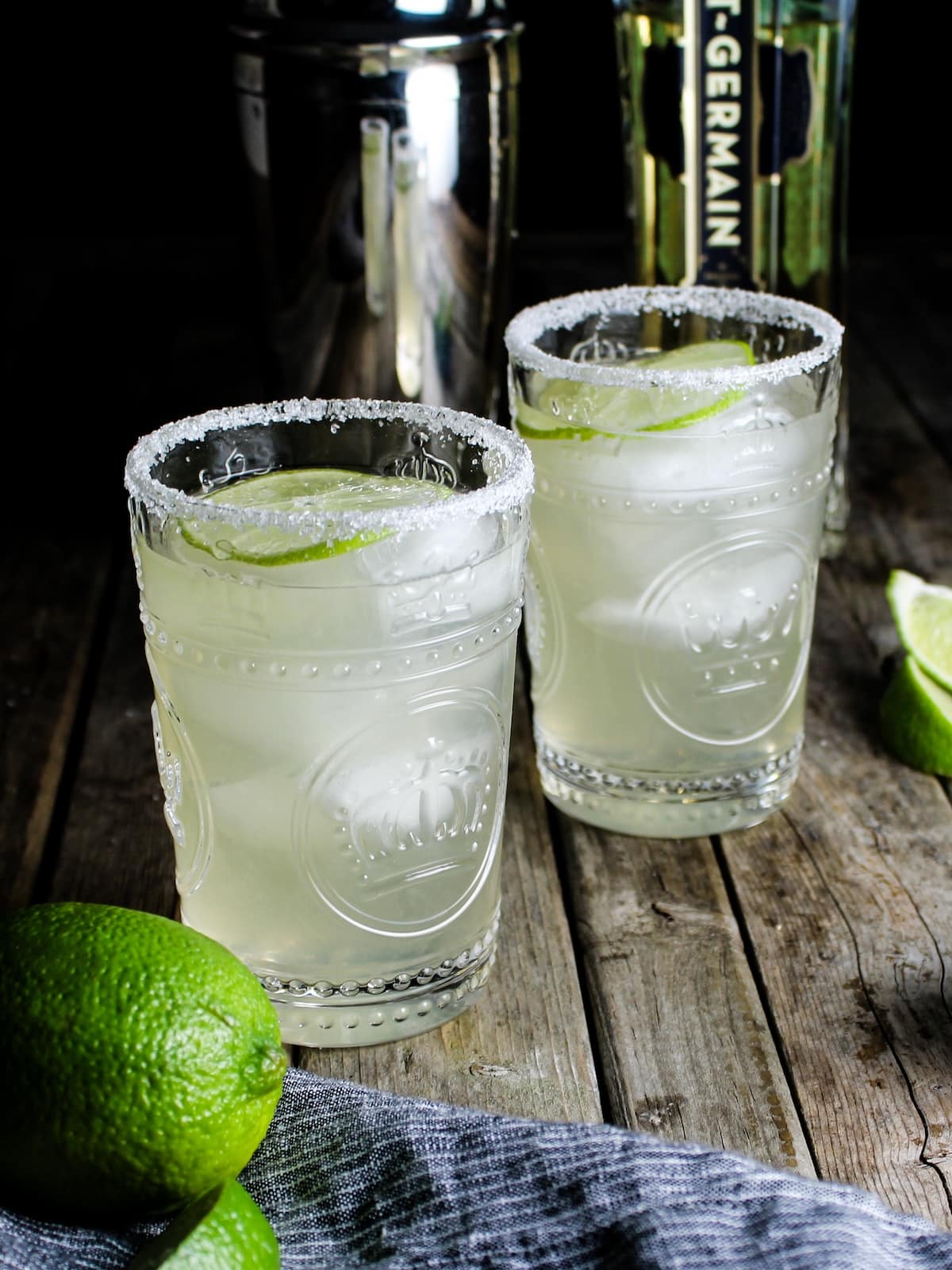 Elderflower Margarita Two Elderflower Margaritas with lime wedges and St. Germain Liqueur in the background.
