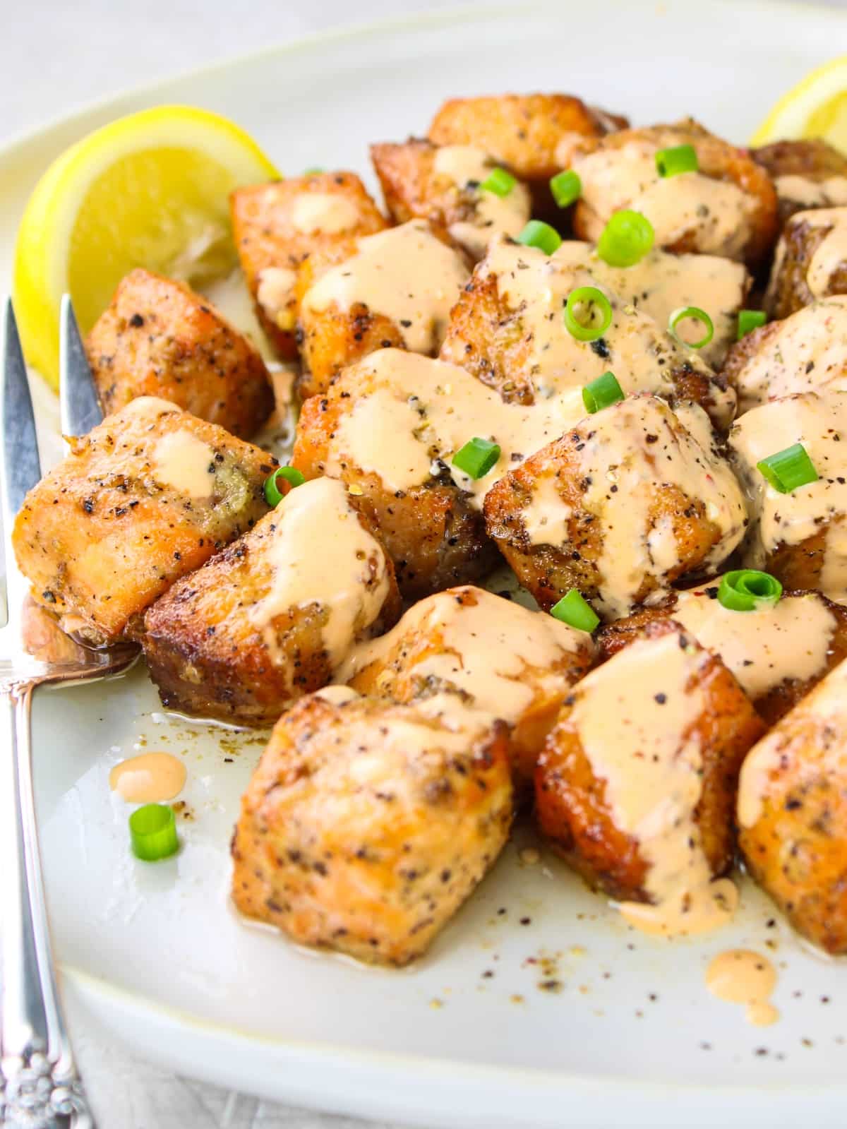 Bang Bang salmon on a plate with lemon wedges and Bang Bang Sauce.