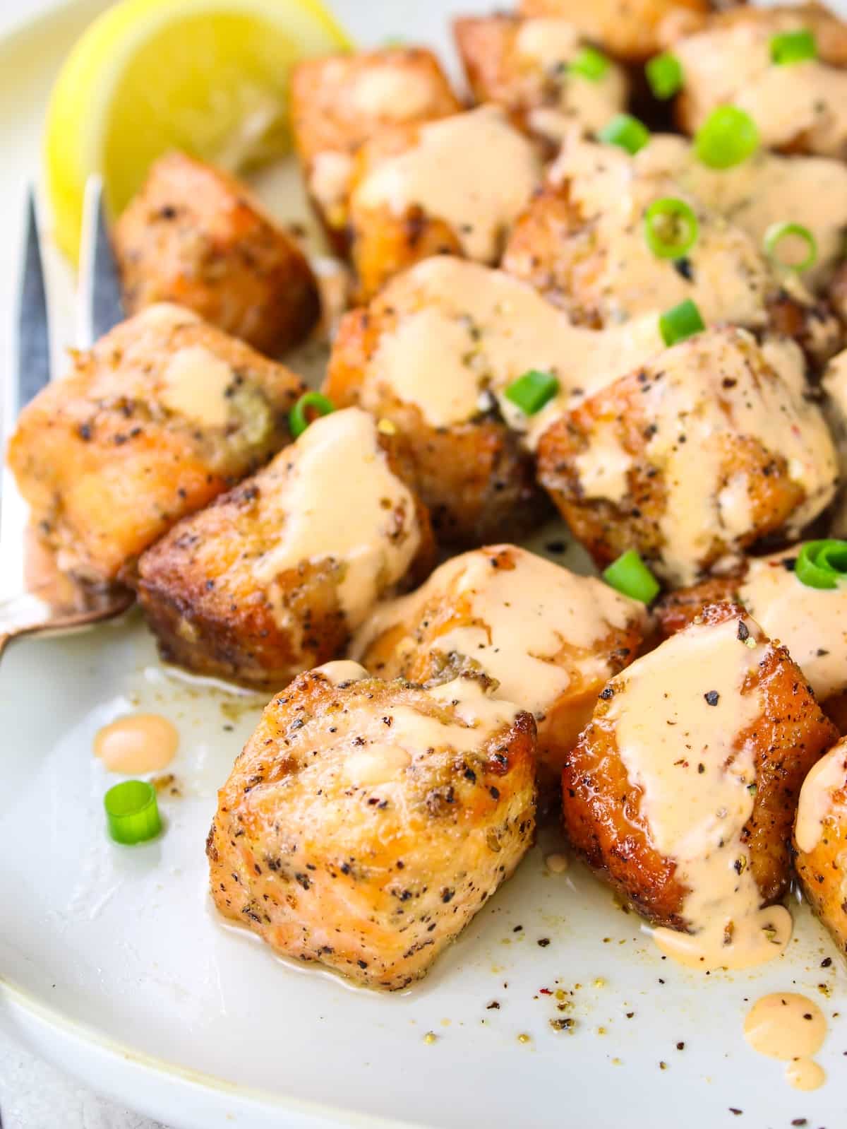 Bang Bang salmon bites on a plate with lemon wedges.
