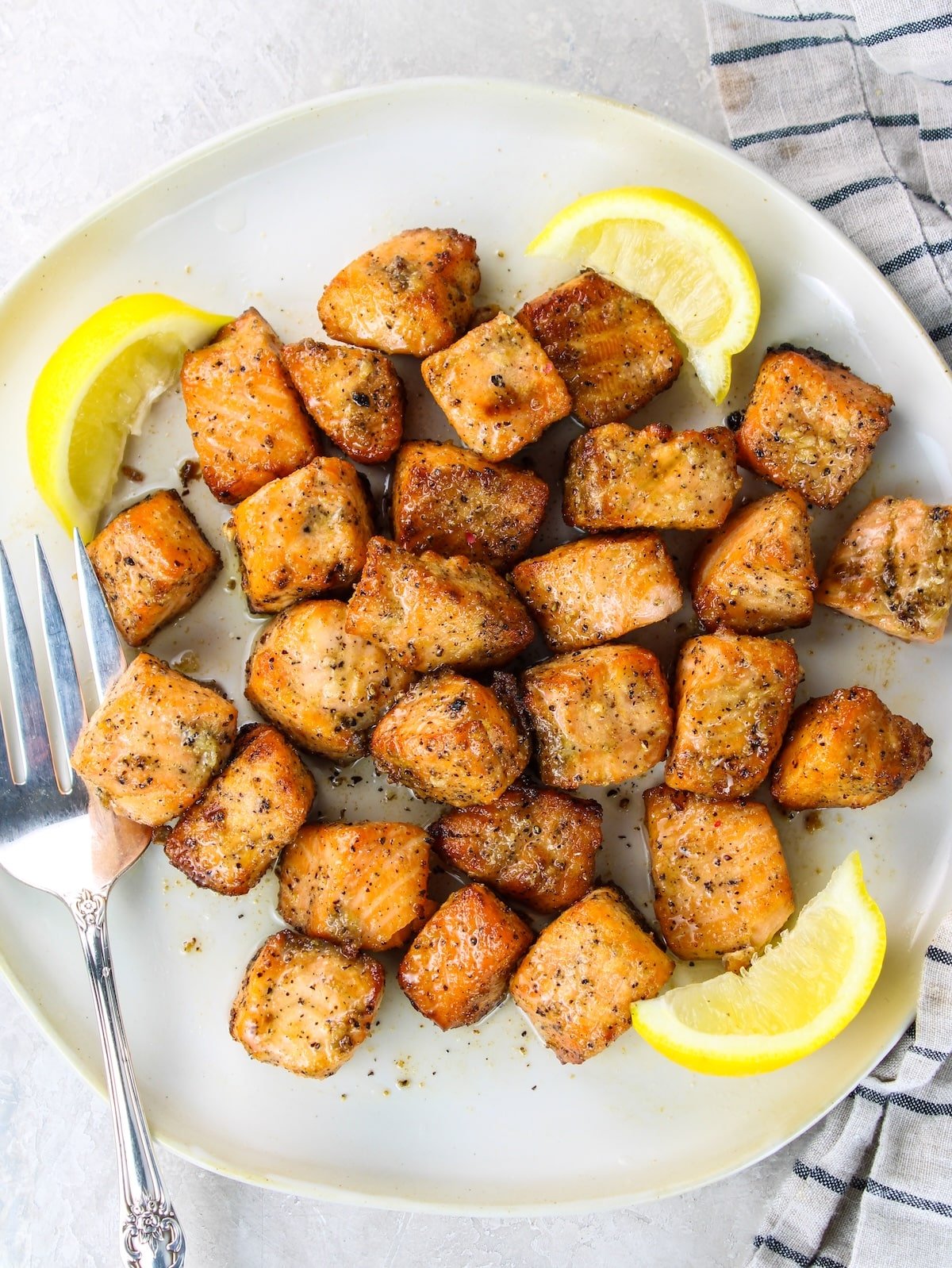 Air fried salmon on a plate with lemon wedges.
