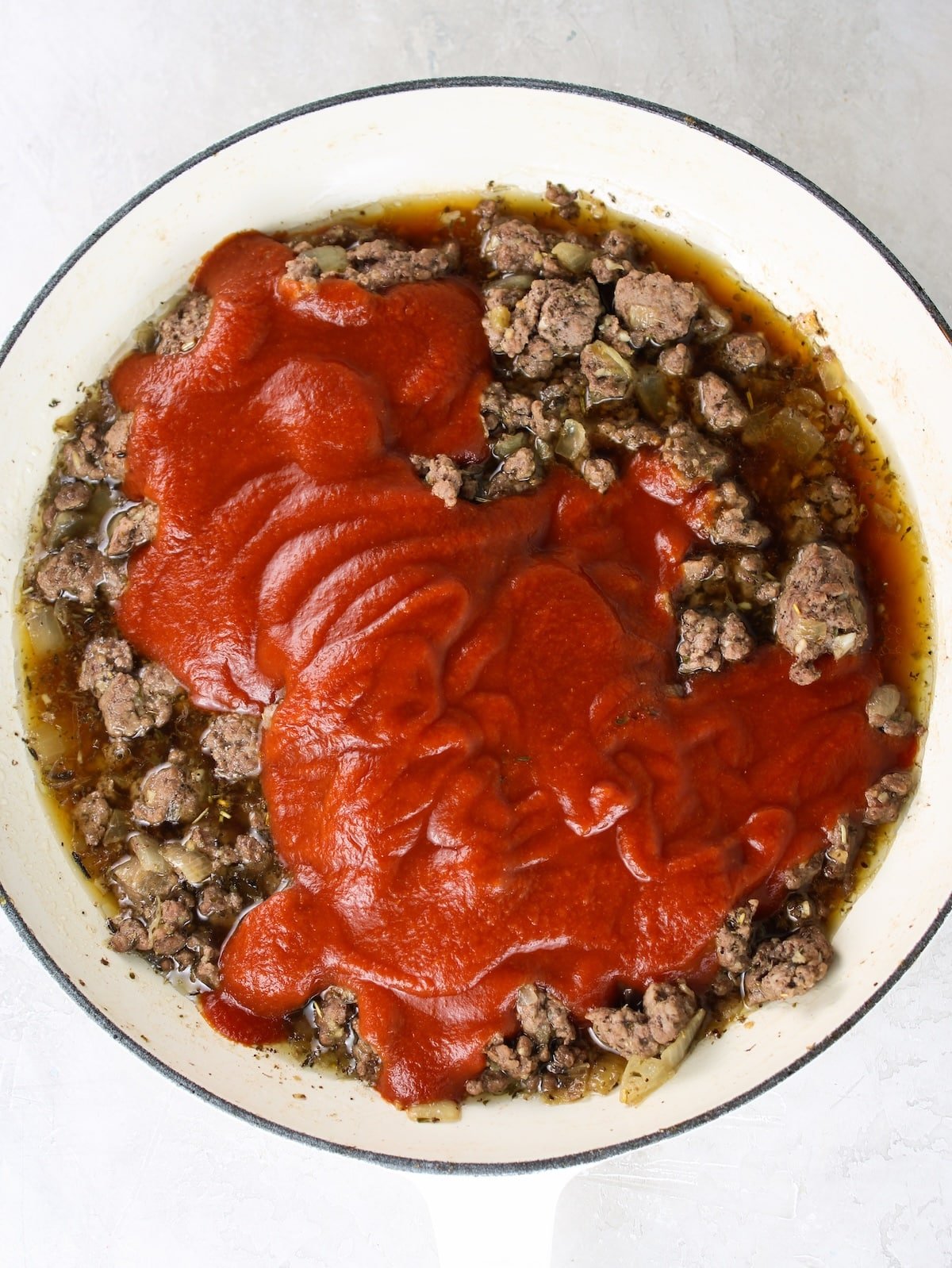Adding tomato sauce to the cooked ground beef mixture.