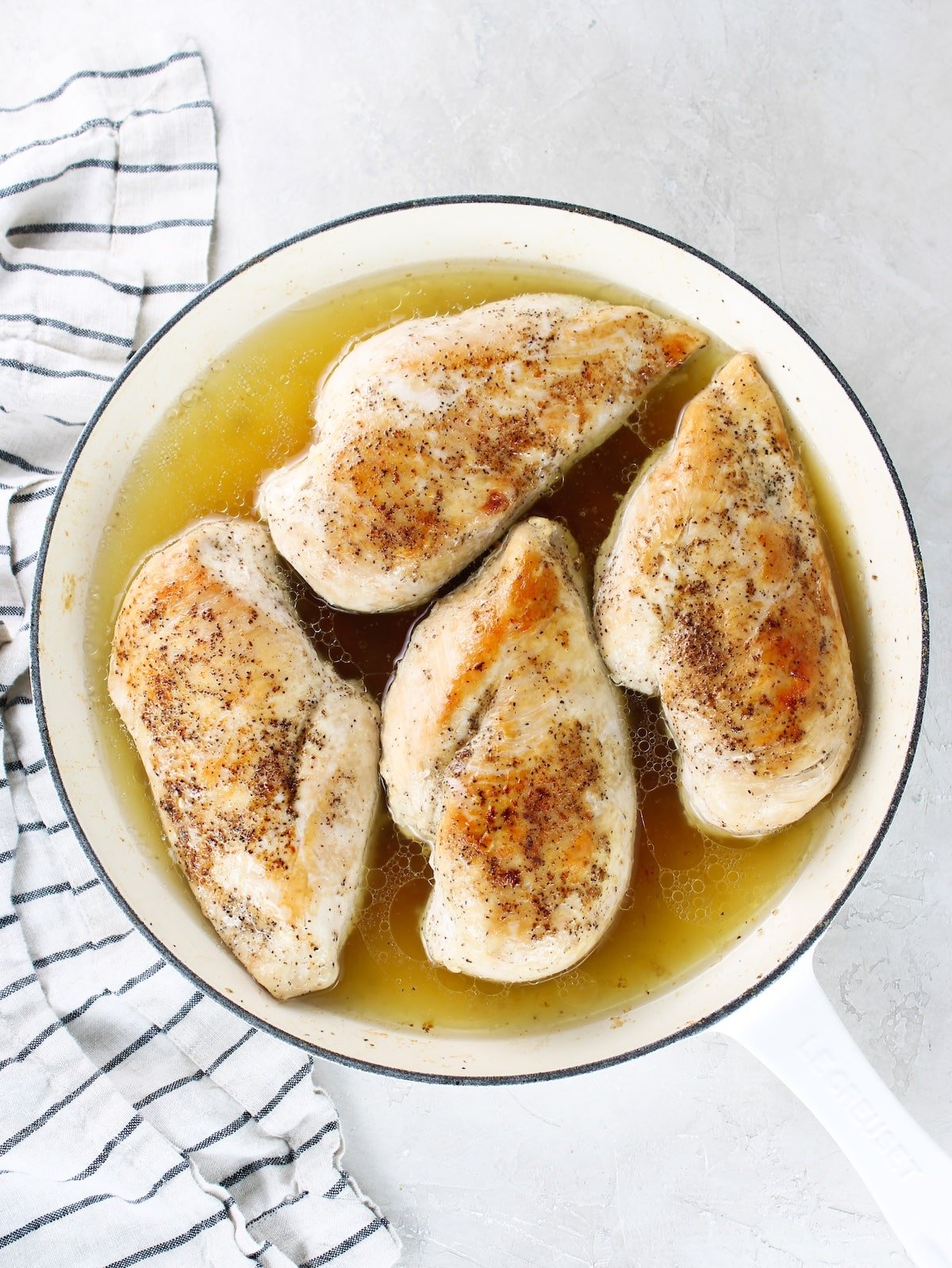 A skillet with seared chicken breasts and chicken stock added to steam chicken.