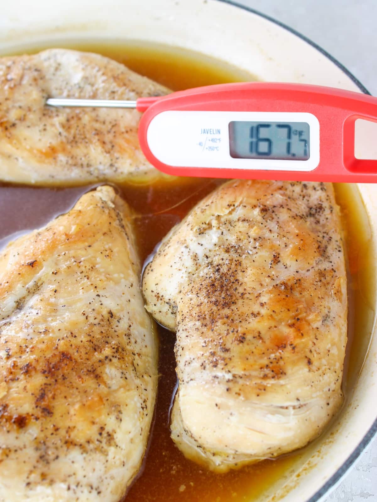 How to Make Juicy Shredded Chicken - a close up photo of three chicken breasts that have been seared and steamed in a skillet on the stovetop with a digital meat thermometer in one breast reading 167 degrees.