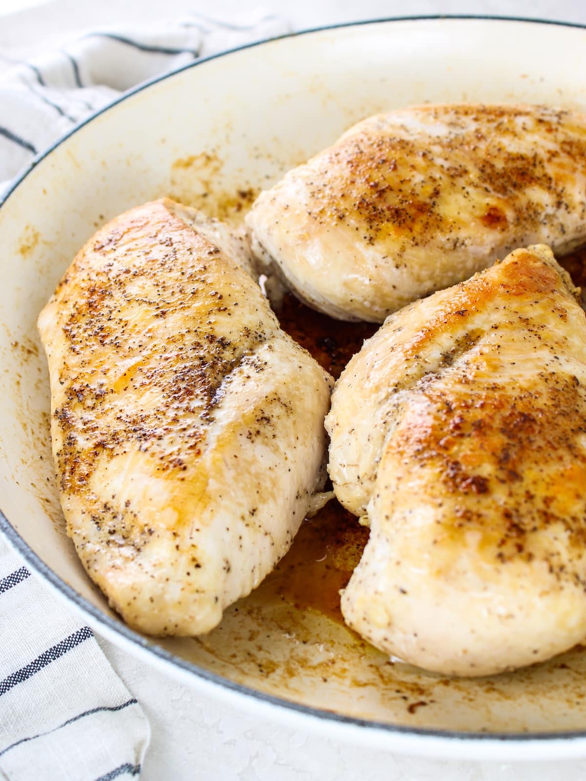 How to Make Juicy Shredded Chicken - a close up photo of three chicken breasts that have been seared and steamed in a skillet on the stovetop.