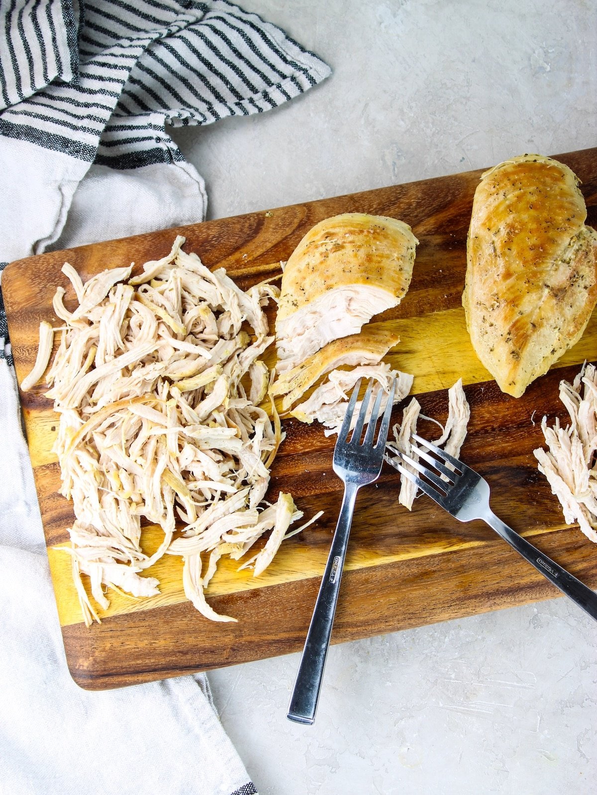 Boneless skinless chicken breasts on a cutting board being shredded with two forks.
