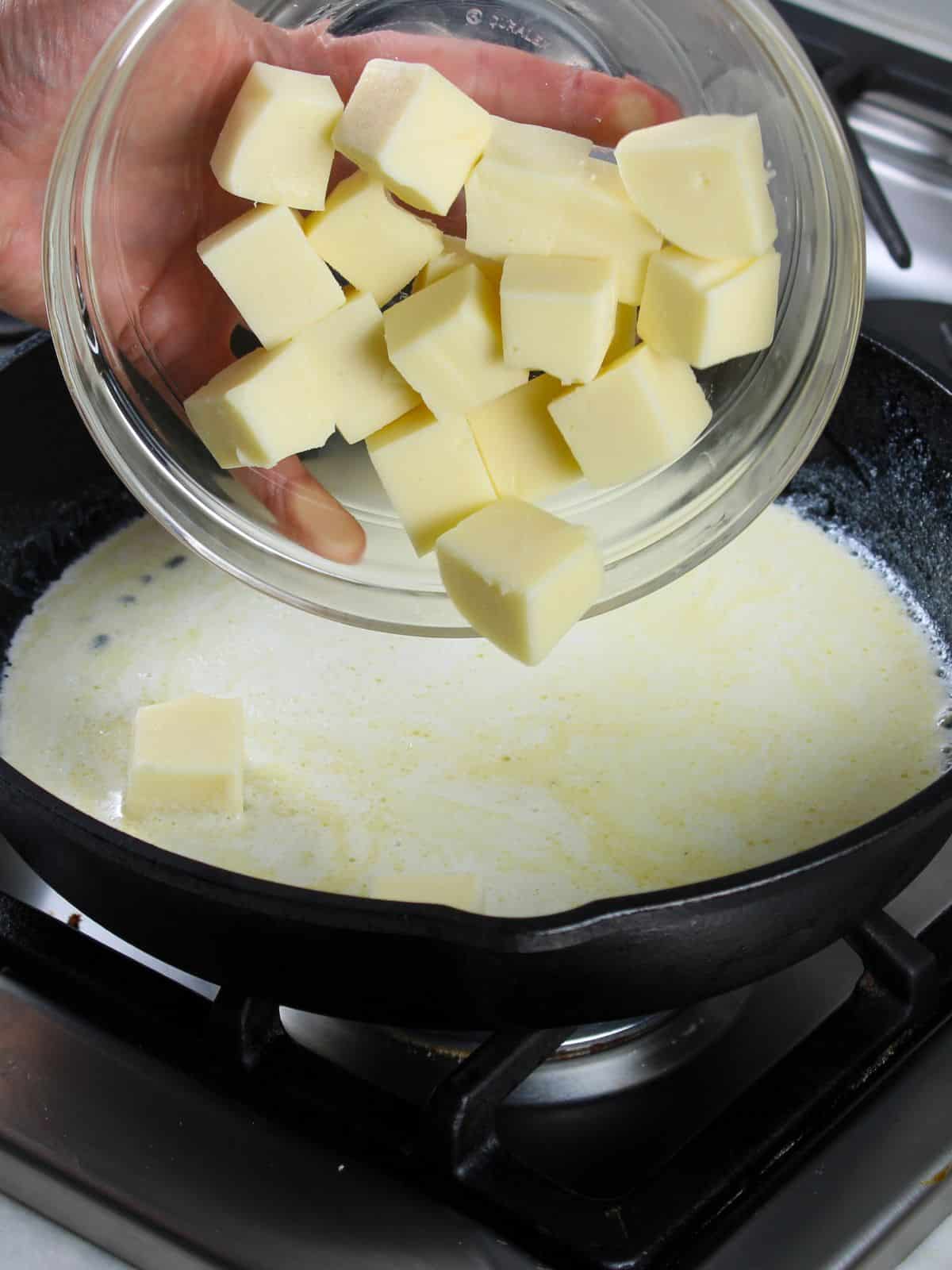 Adding cubes of white cheese to skillet with cream and butter for choripollo.