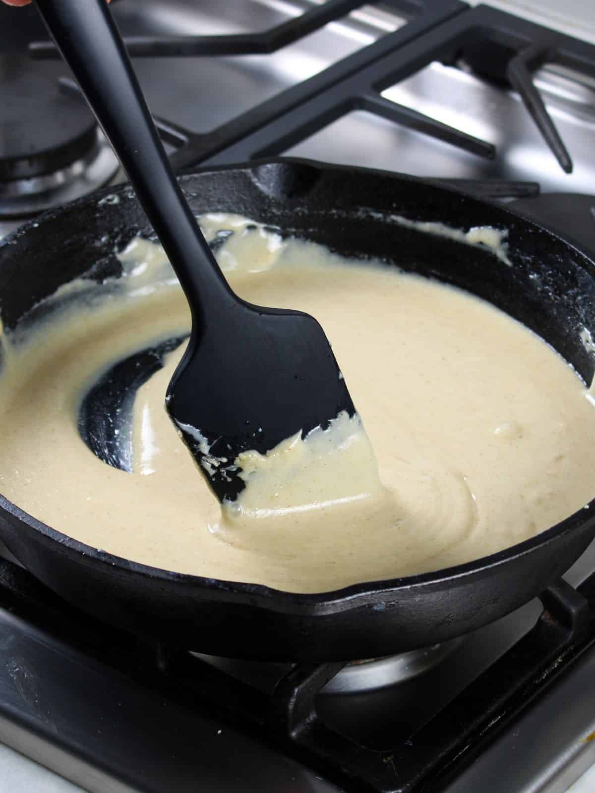 Spatula stirring cheese sauce in cast iron skillet.