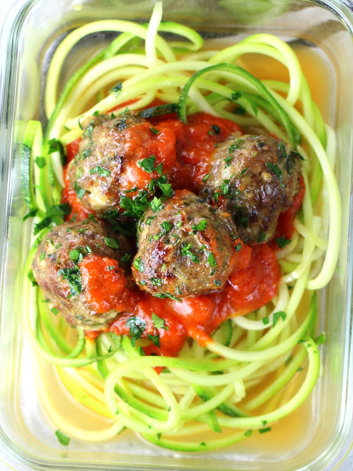 A glass meal prep containers with zucchini noodles, marinara sauce and healthy baked turkey meatballs.