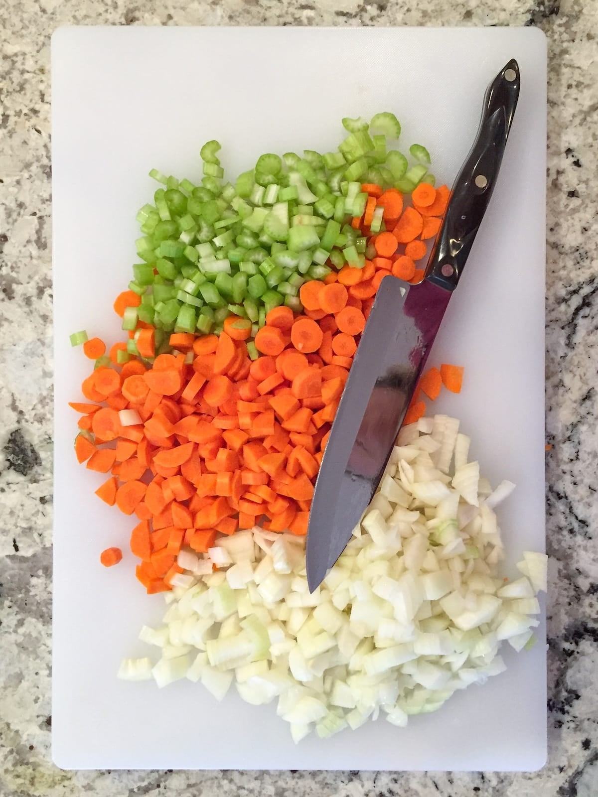 Chopped carrots, onion, and celery on a cutting board.