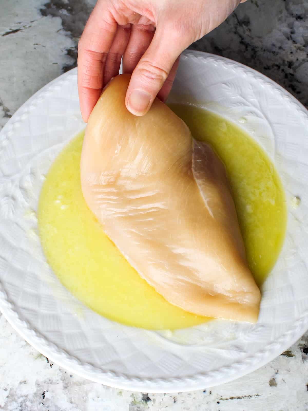 Chicken breast being dipped in garlic-lemon butter for baked Parmesan crusted chicken.