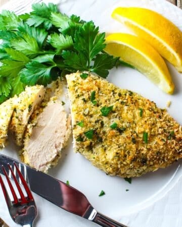 Easy Parmesan crusted chicken sliced on a plate with fresh parsley and lemon wedges, juicy interior and golden coating.