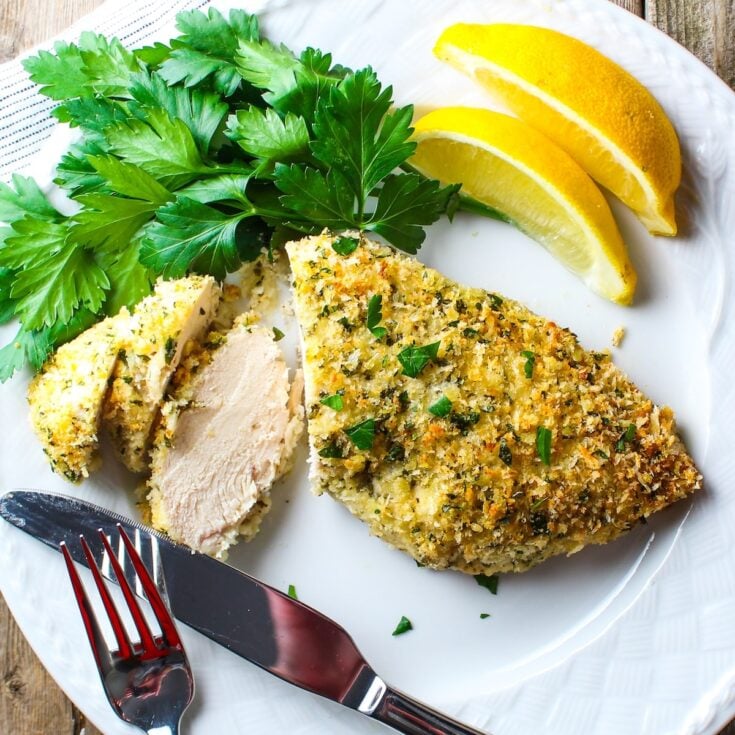Easy Parmesan crusted chicken sliced on a plate with fresh parsley and lemon wedges, juicy interior and golden coating.