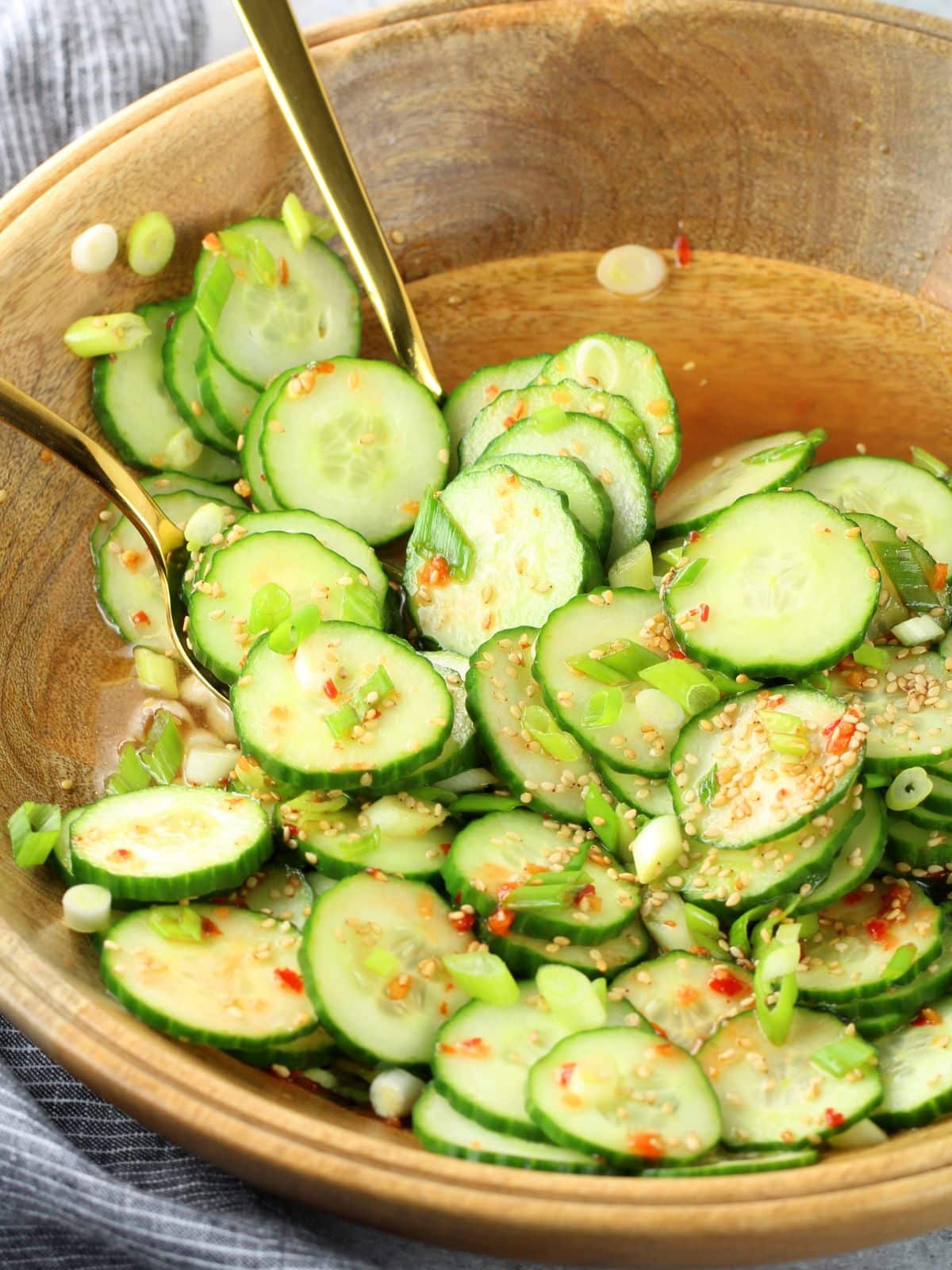 Asian cucumber salad with sesame oil, rice vinegar, chili garlic sauce, and green onions in a white bowl — a light and refreshing BBQ side dish