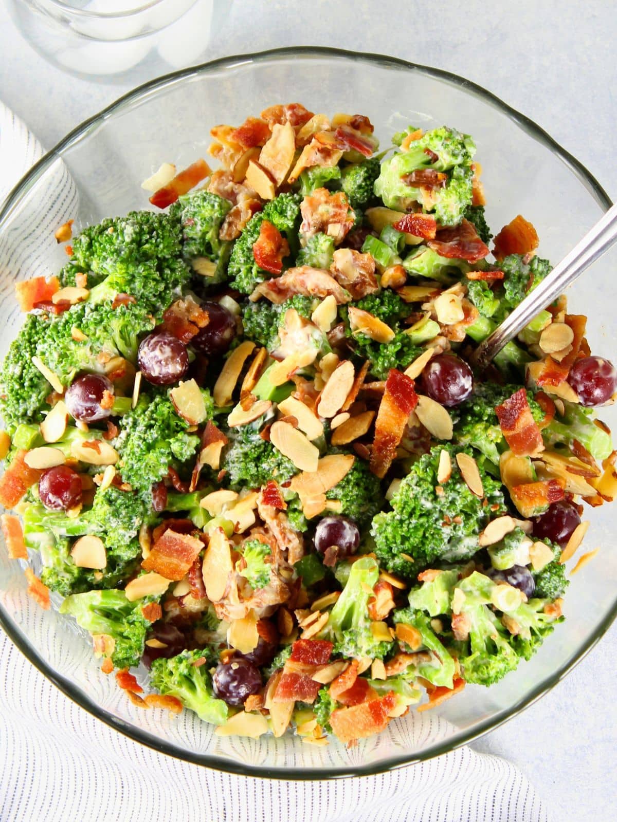 Broccoli salad with red grapes, crispy bacon, toasted almonds, and creamy dressing in a glass bowl — a sweet and savory BBQ side