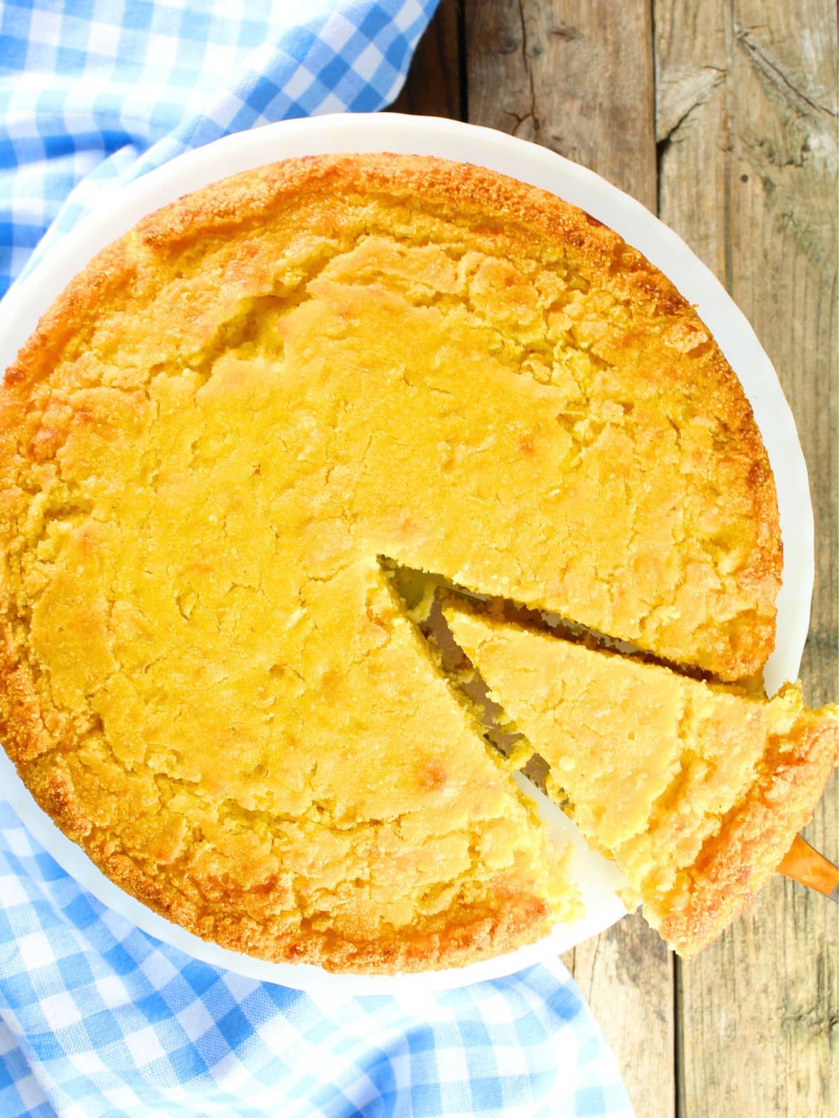 Moist Caribbean cornbread with a golden crust in a white pie dish with one slice being lifted out — a unique and crowd-pleasing BBQ side