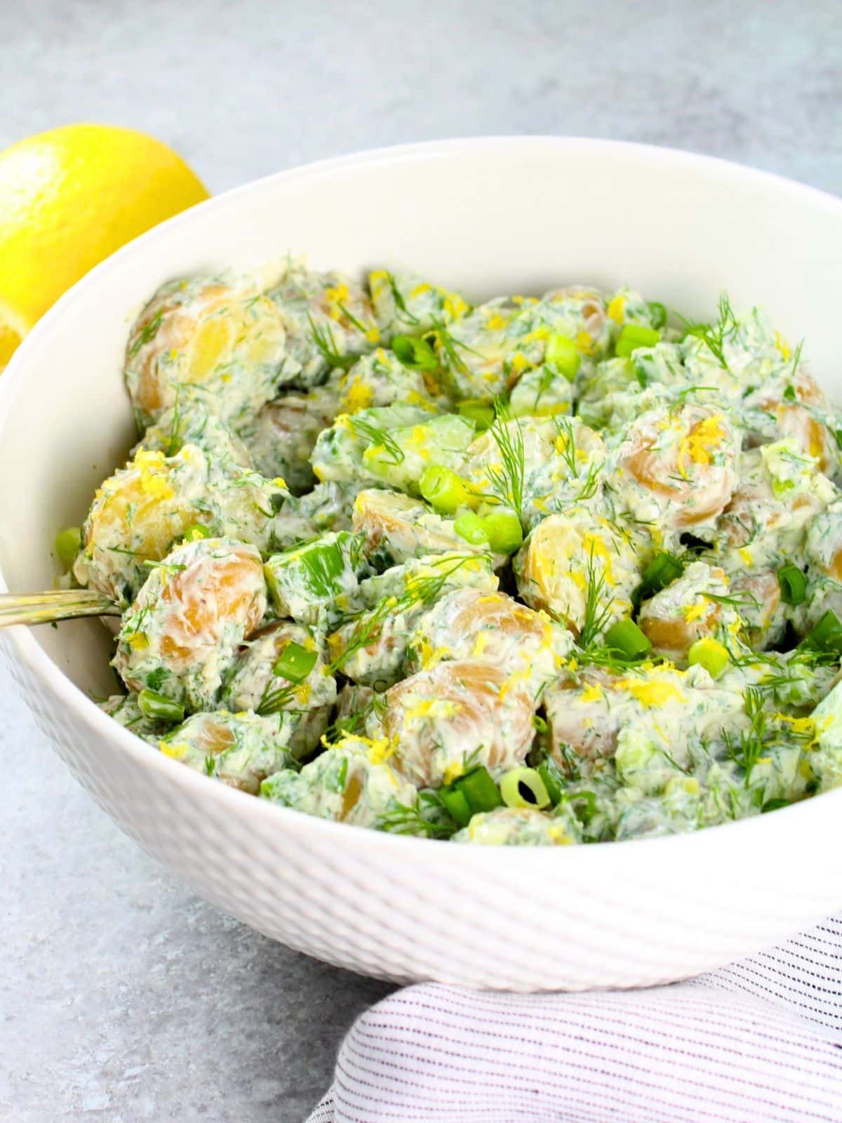 Greek tzatziki potato salad with baby potatoes, cucumber, dill, and lemon in a white bowl — a light no-mayo BBQ side