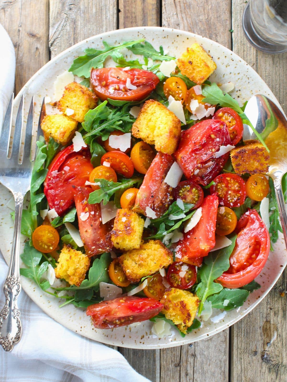 Heirloom tomato cornbread salad with colorful tomatoes, crispy cornbread croutons, arugula, and shaved Parmesan on a white platter