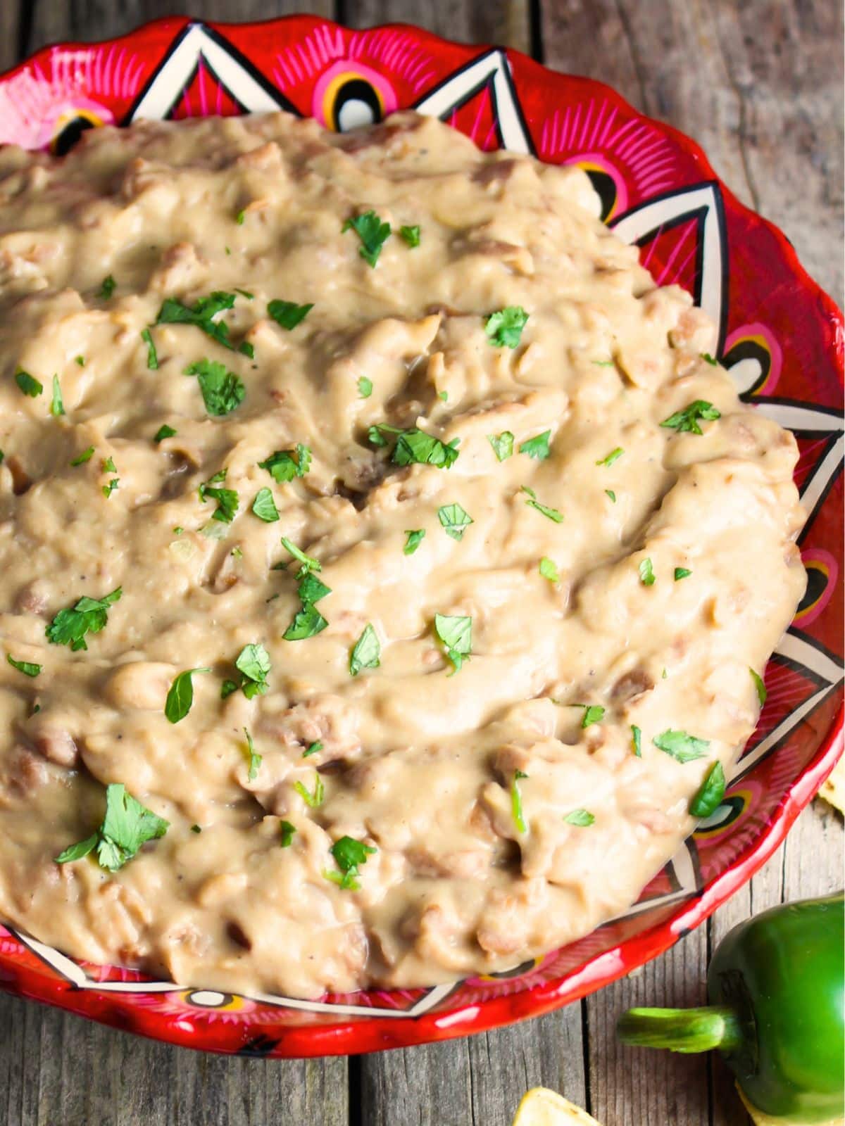 Homemade refried beans in a white bowl with melted cheddar cheese and cilantro — a creamy and delicious BBQ side dish