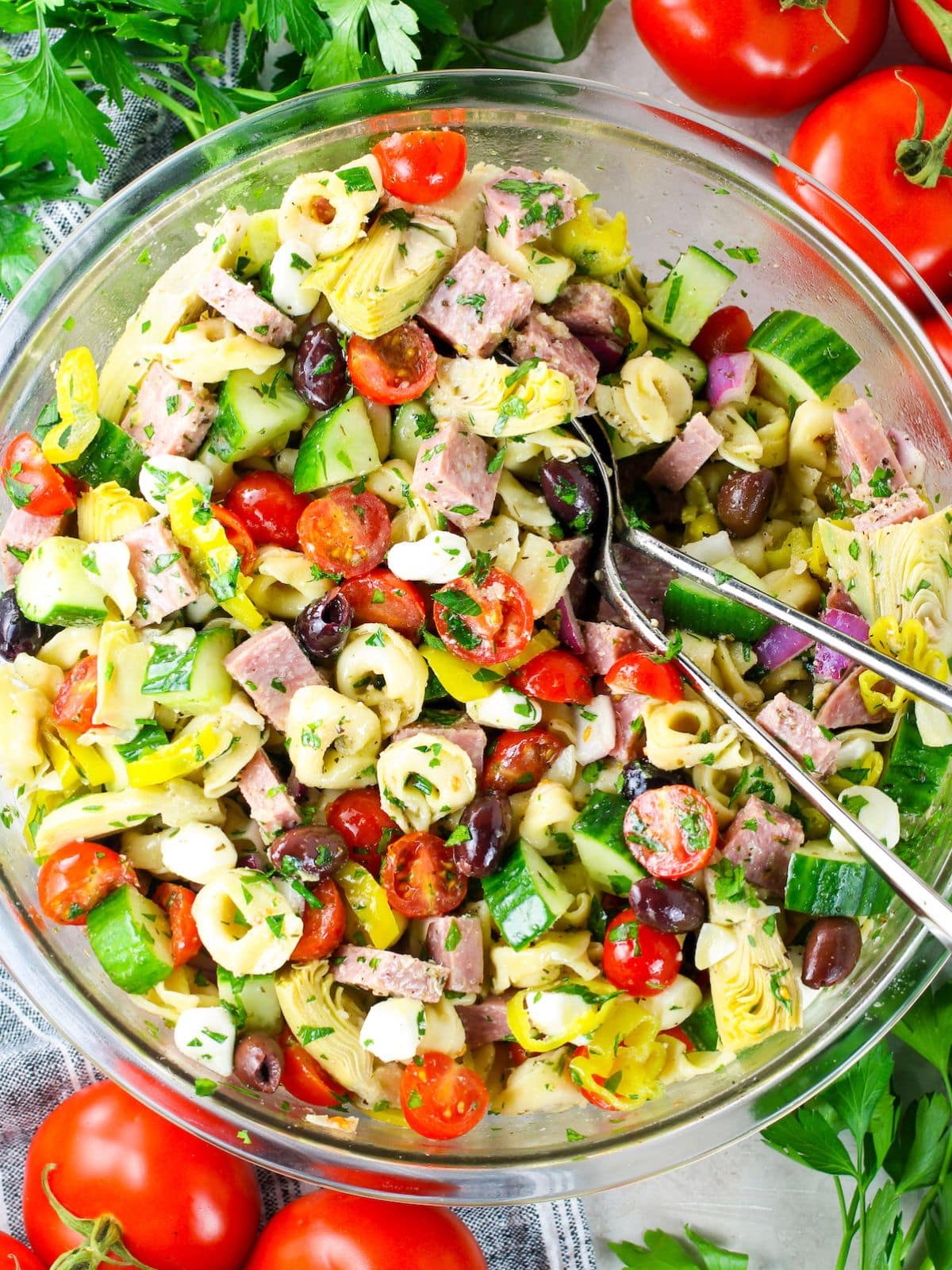 Colorful Italian tortellini pasta salad with cherry tomatoes, cucumber, salami, olives, and mozzarella in a glass bowl — one of the best BBQ side dishes
