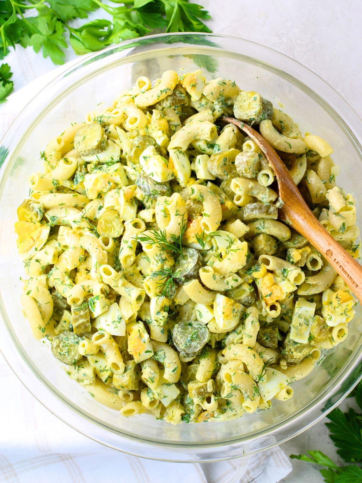 Creamy macaroni salad with dill pickles, hard boiled eggs, and fresh dill in a large glass bowl — a classic BBQ side dish