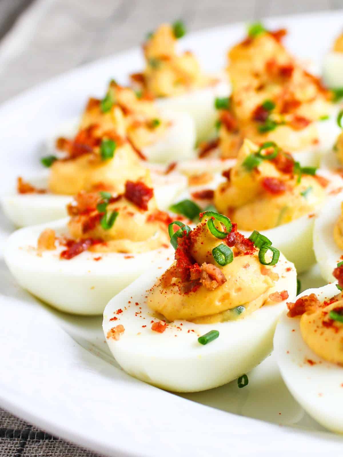 Smoky deviled eggs topped with crispy bacon and smoked paprika on a white serving platter — an easy make-ahead BBQ appetizer