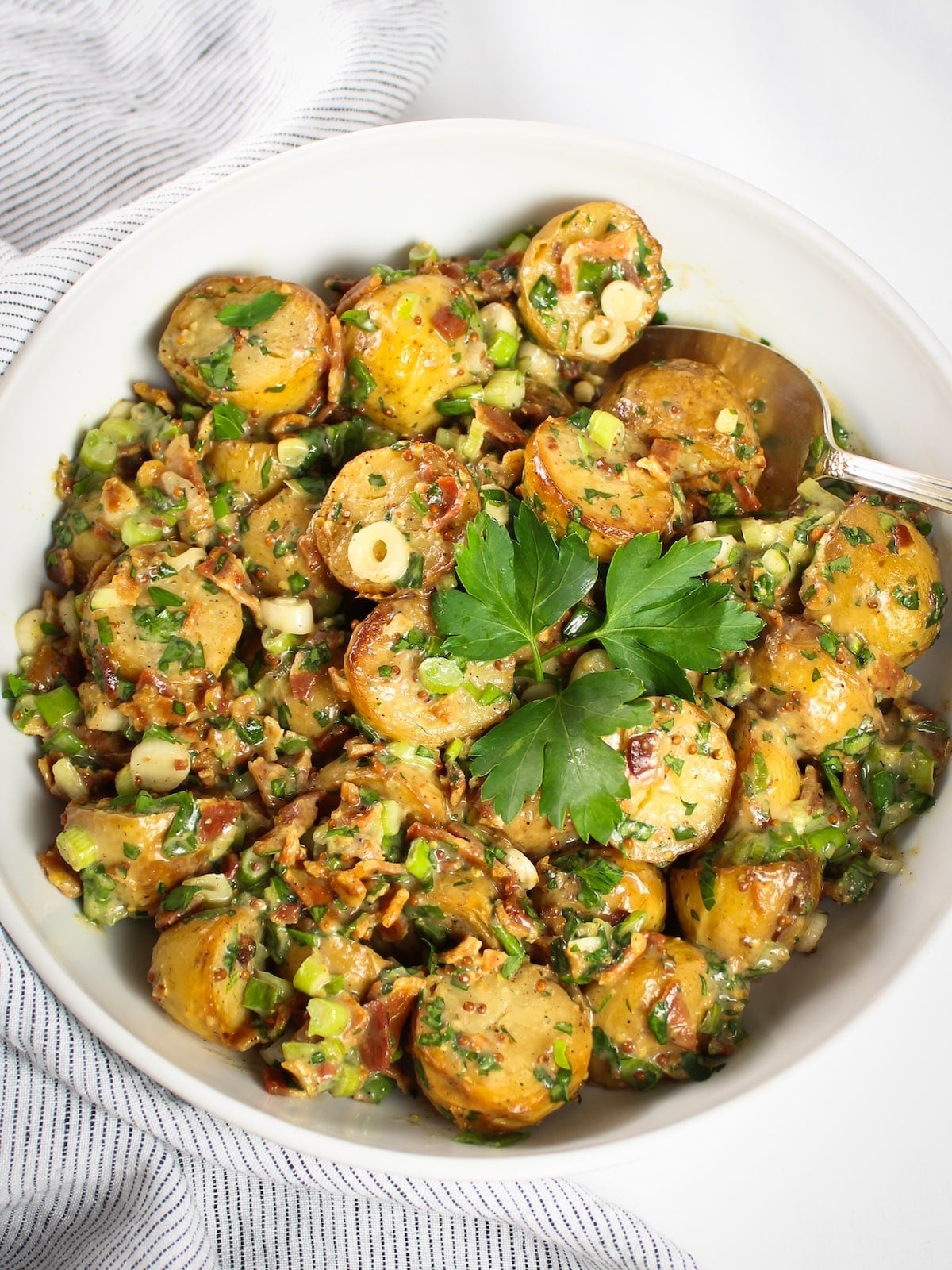 Smoky salt and vinegar potato salad with tender potatoes in a tangy dressing with fresh herbs in a white bowl