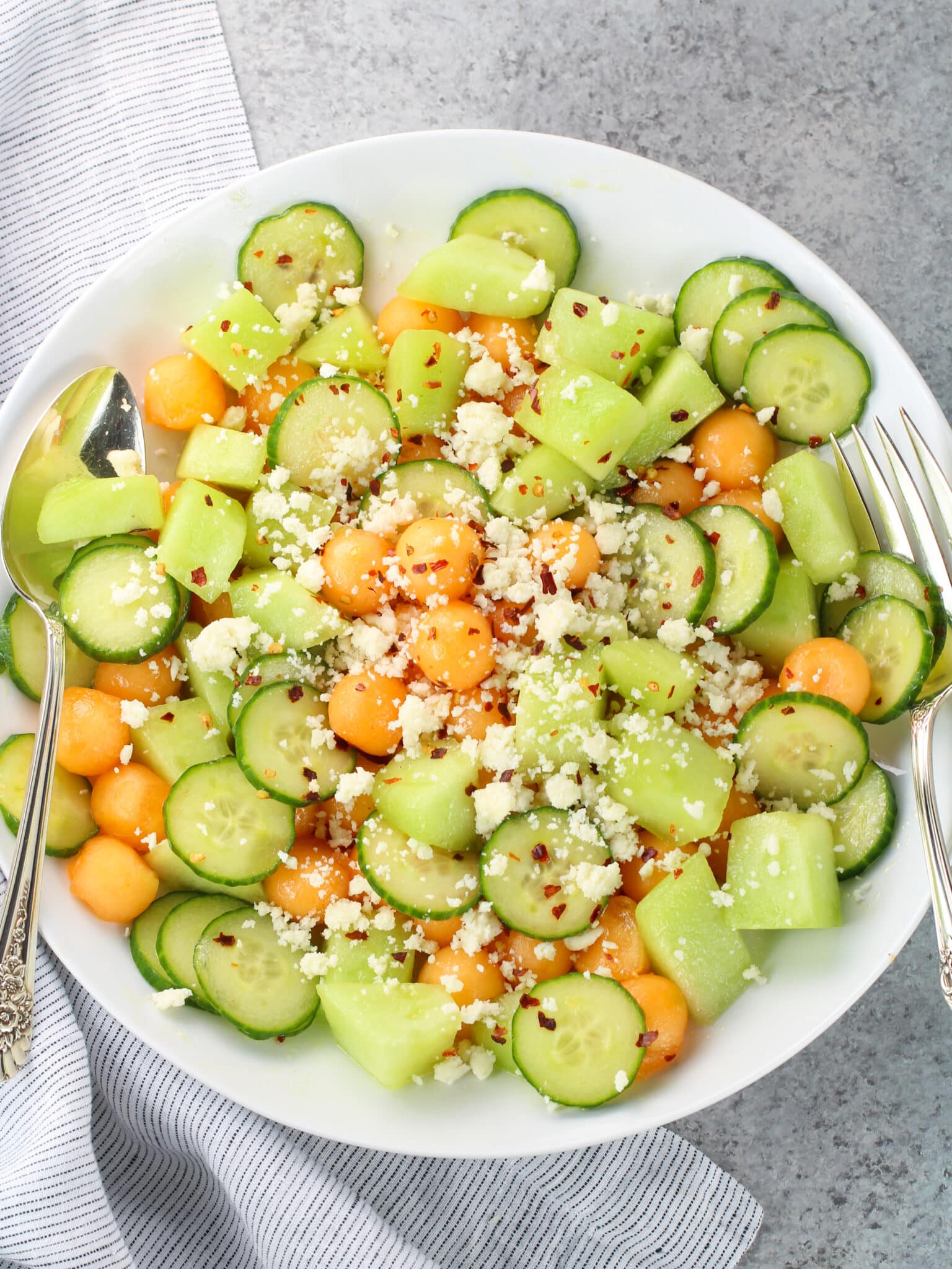 Summer melon salad with cantaloupe, honeydew, cucumber, and crumbled feta on a white platter with a honey lime dressing