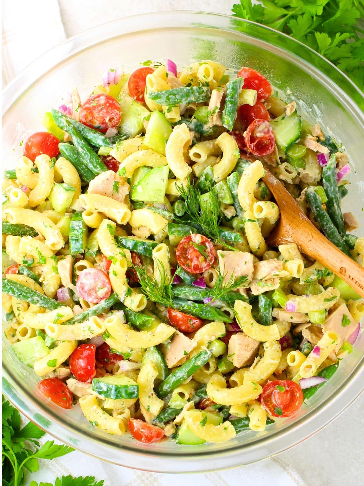 Tuna pasta salad with green beans, cucumber, cherry tomatoes, and a creamy herb dressing in a large glass bowl — an easy BBQ side dish