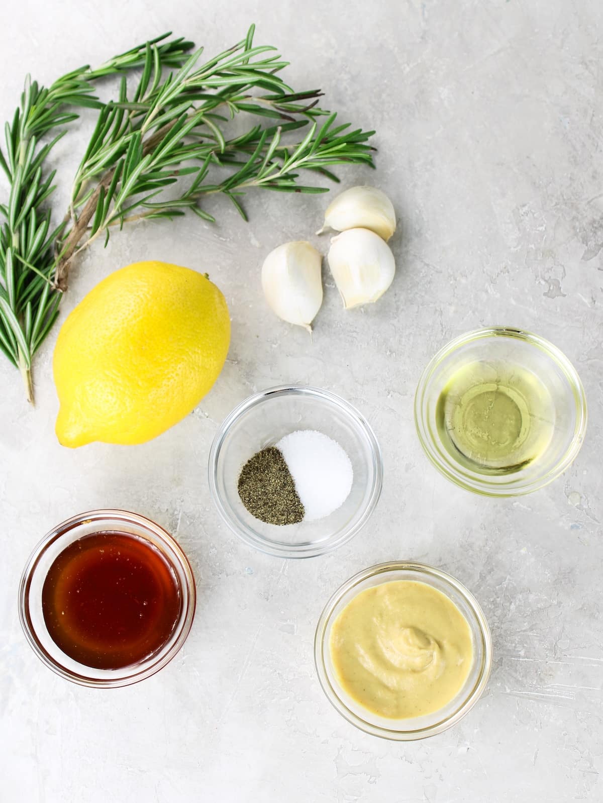 Honey, lemon, Dijon mustard, garlic, olive oil, rosemary, salt and pepper arranged on a light surface for a chicken thigh marinade