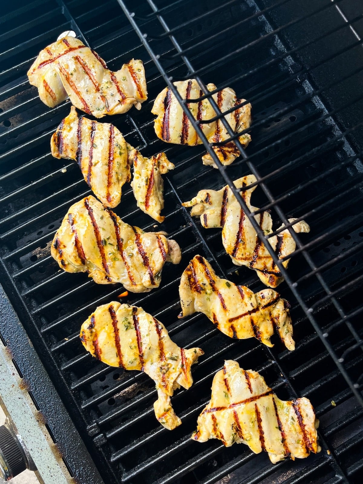 Boneless chicken thighs with rosemary lemon marinade cooking on a gas grill, overhead view showing grill marks forming