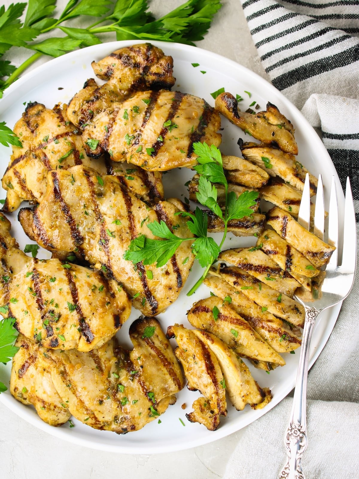 Overhead shot of grilled chicken thighs with rosemary lemon marinade on a white plate with serving forks and fresh parsley