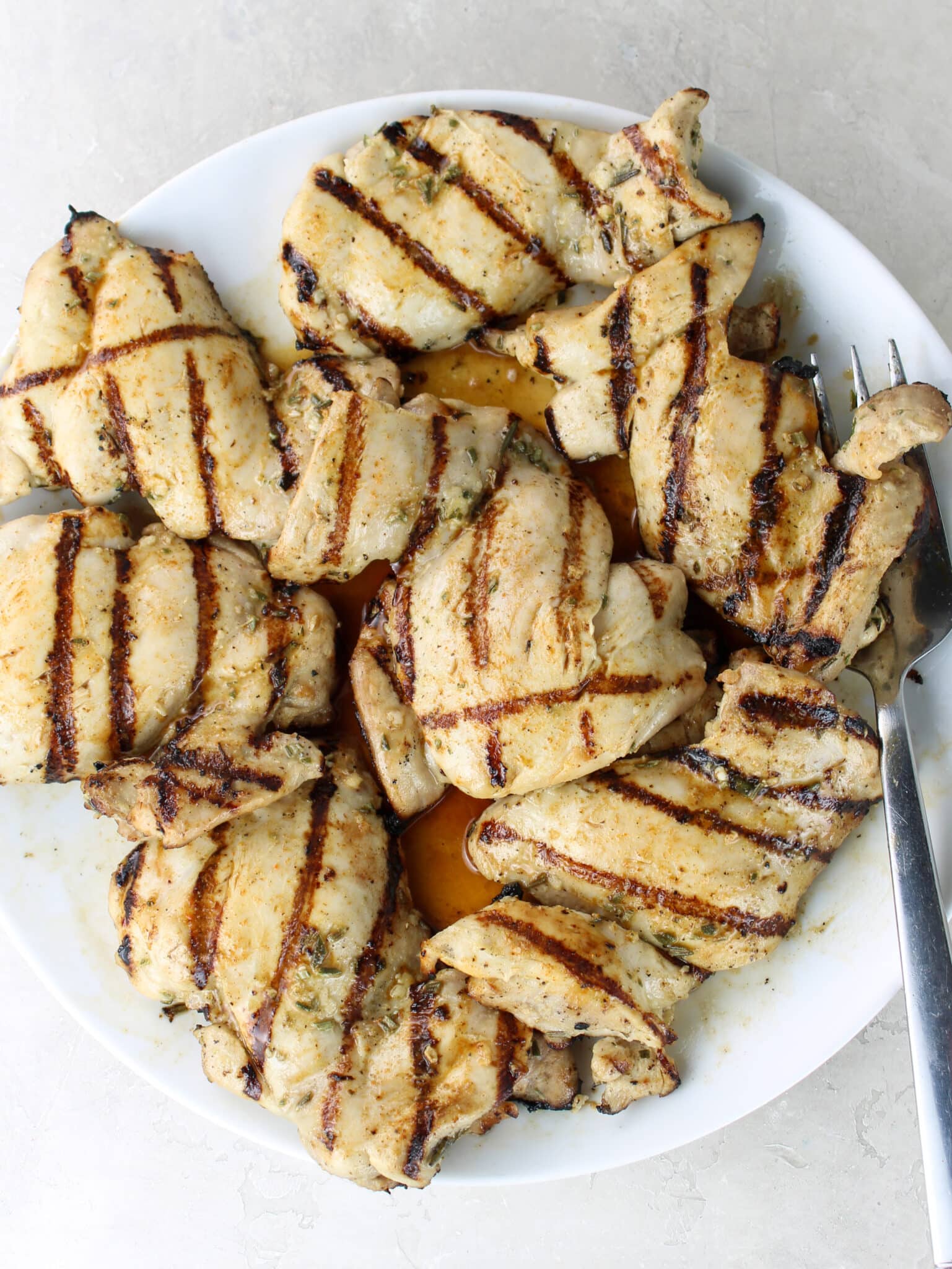 Juicy grilled chicken thighs with golden grill marks piled on a white plate with a serving fork