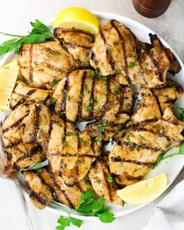 Juicy grilled chicken thighs with rosemary lemon marinade on a white plate with lemon wedges and fresh parsley