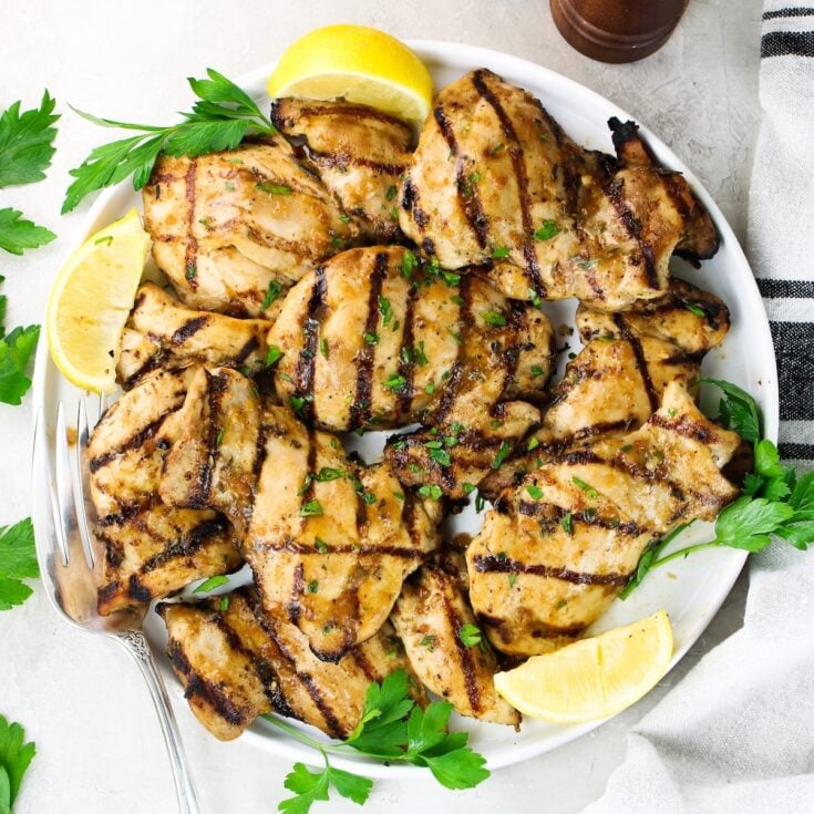 Juicy grilled chicken thighs with rosemary lemon marinade on a white plate with lemon wedges and fresh parsley