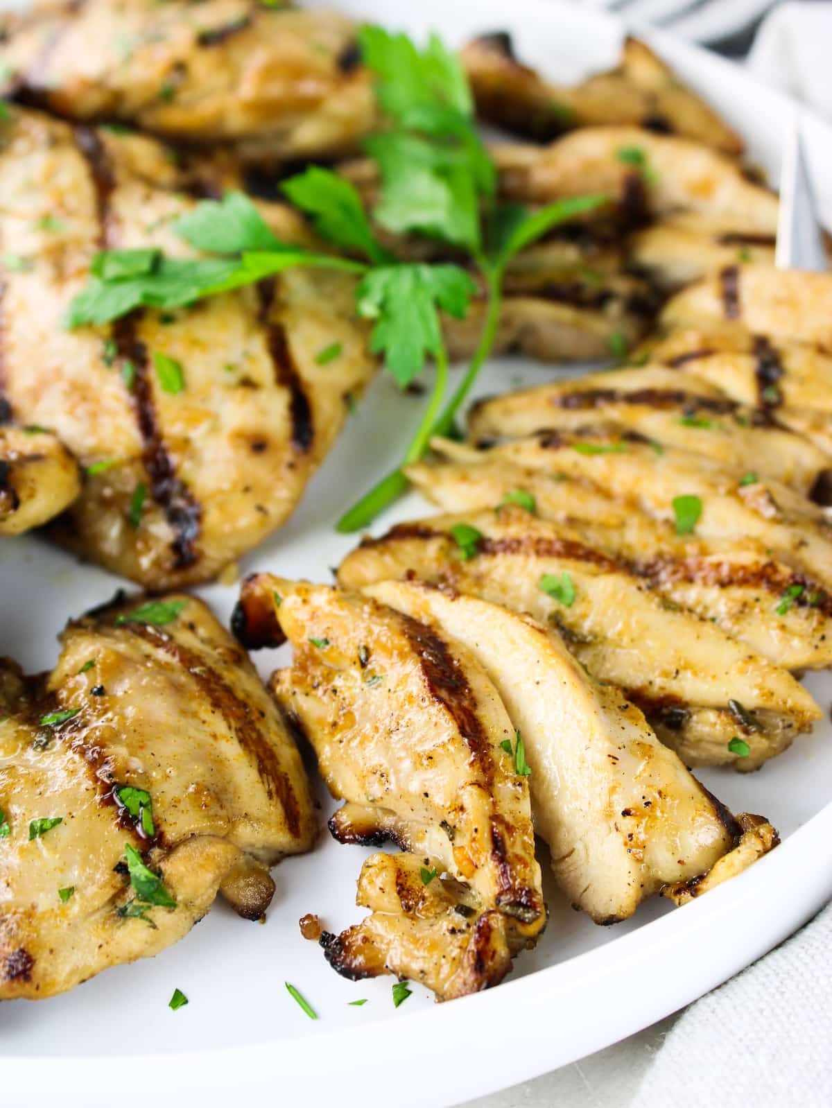 Close-up of juicy grilled chicken thighs sliced and garnished with fresh parsley on a white plate