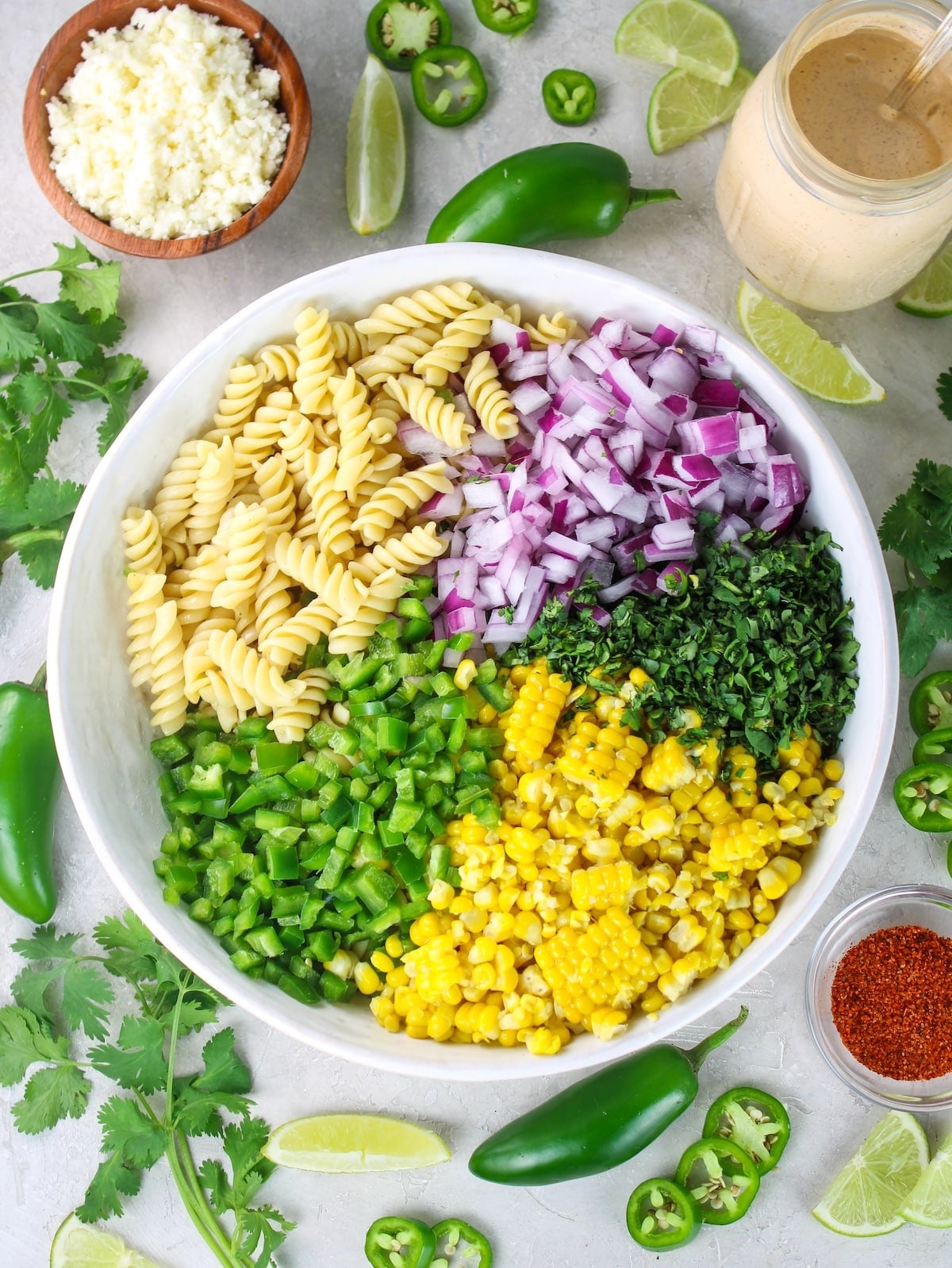 Ingredients for Mexican street corn pasta salad including rotini pasta, corn, jalapeño, red onion, cilantro, cotija, and chili-lime dressing